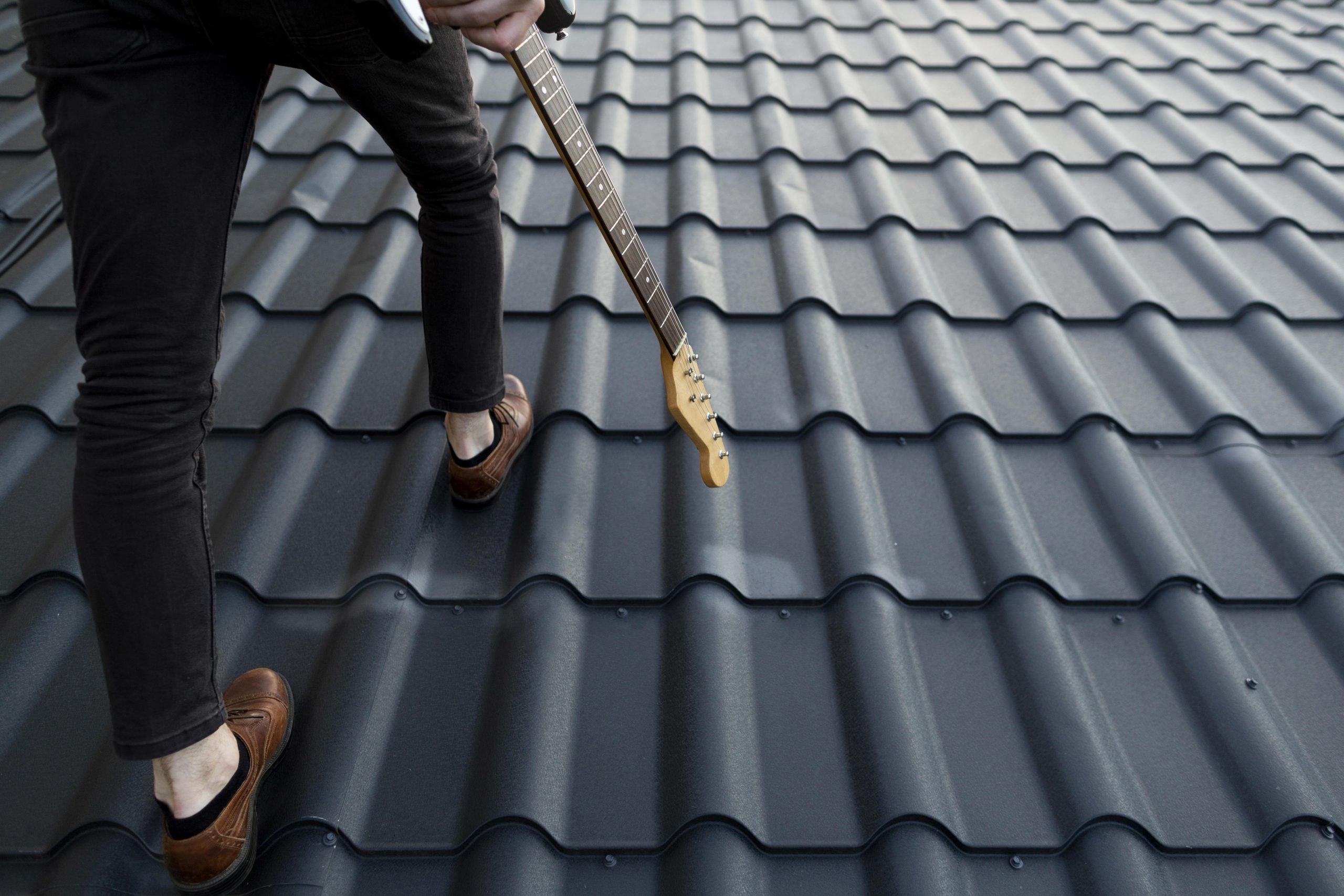 back-view-male-musician-climbing-roof-with-electric-guitar